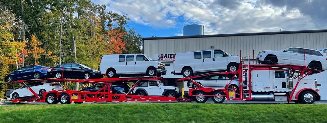 Baier Transport car carrier loaded with Chevy Express vans and sedans with New England fall foliage — seasonal snowbird auto transport from NH to Florida